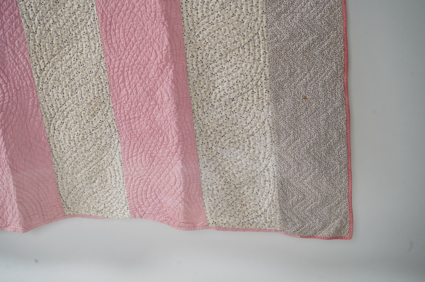 An English 19th century, highly ornate hand quilted English bedcover. Designed using alternating stripes, in a plain pink and a small printed floral cotton, then finishing with two borders of a darker minute spot floral